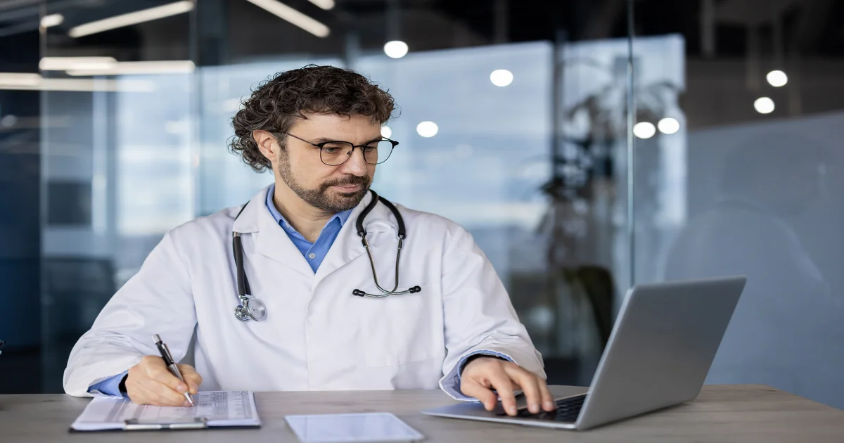 Médico focado trabalhando no laptop em clínica — cálculo do Fator R